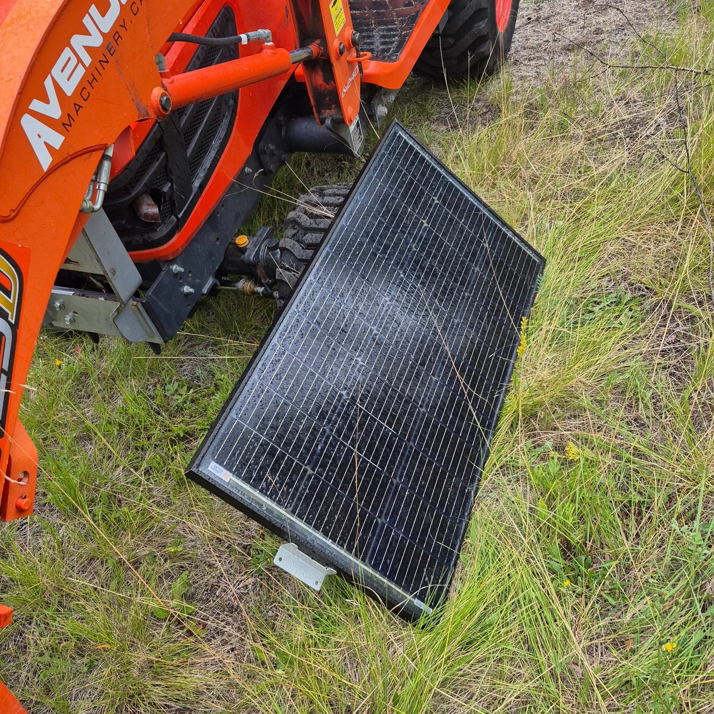 Solar panel on the ground next to an orange tractor in a grassy area