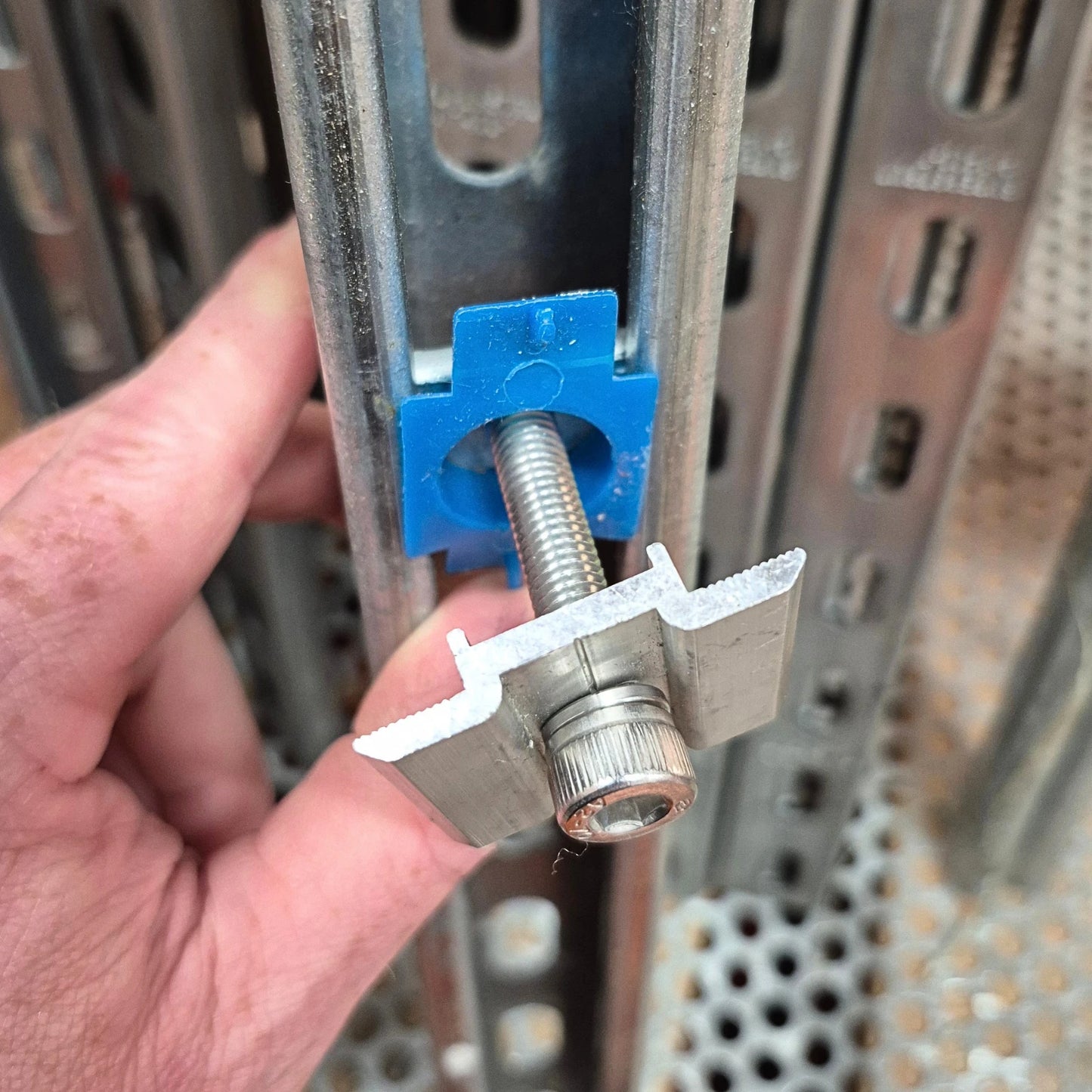 hand holding a metal solar panel clamp installed in a metal channel