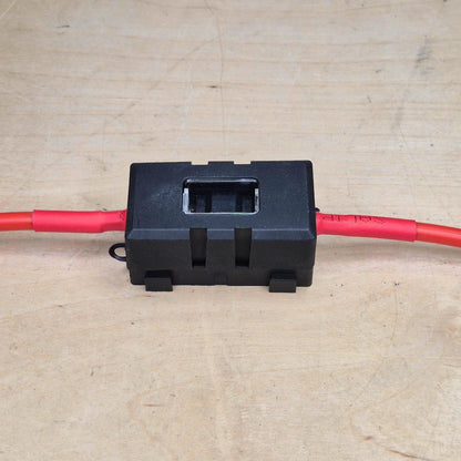 Black electrical midi fuse holder with red wires on a beige background