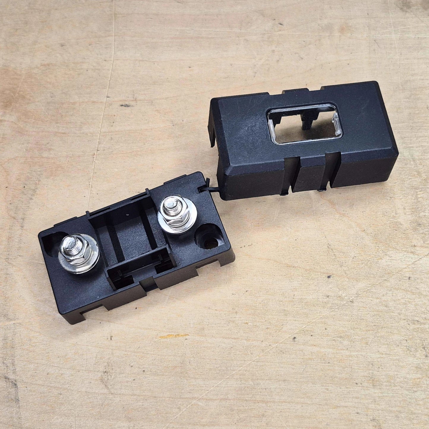 Two black plastic components with metallic bolts on a beige surface