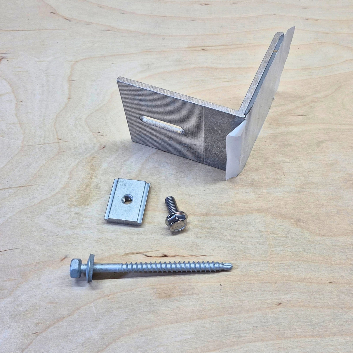 Kinetic Solar Universal L bracket with butyl seal on a wood background.  Shown with included screw and bolt hardware.