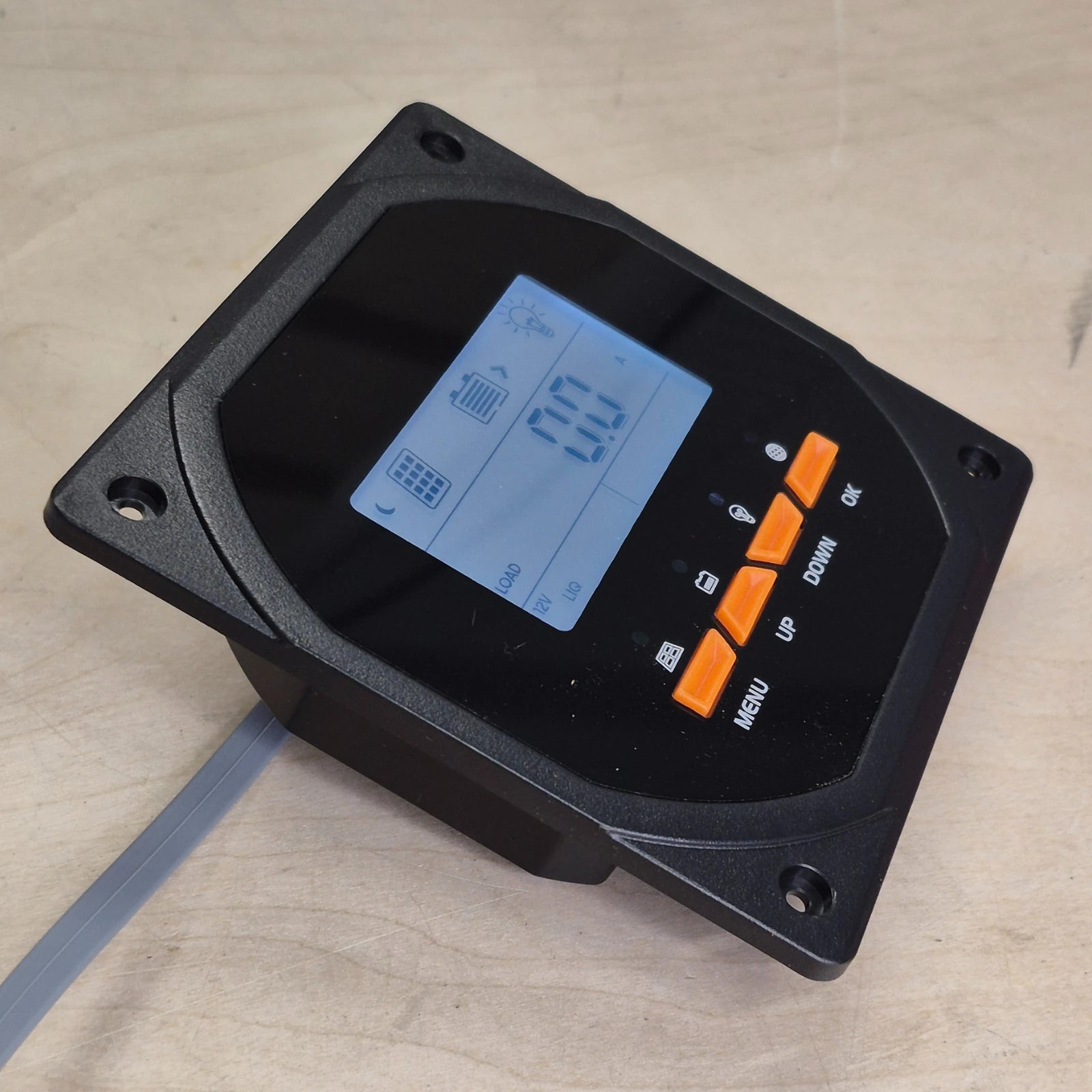 Digital control panel with a blue display and orange buttons on a wood surface