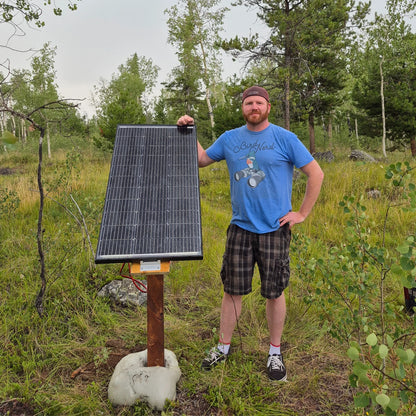 Man holding a solar panel in a forested area
