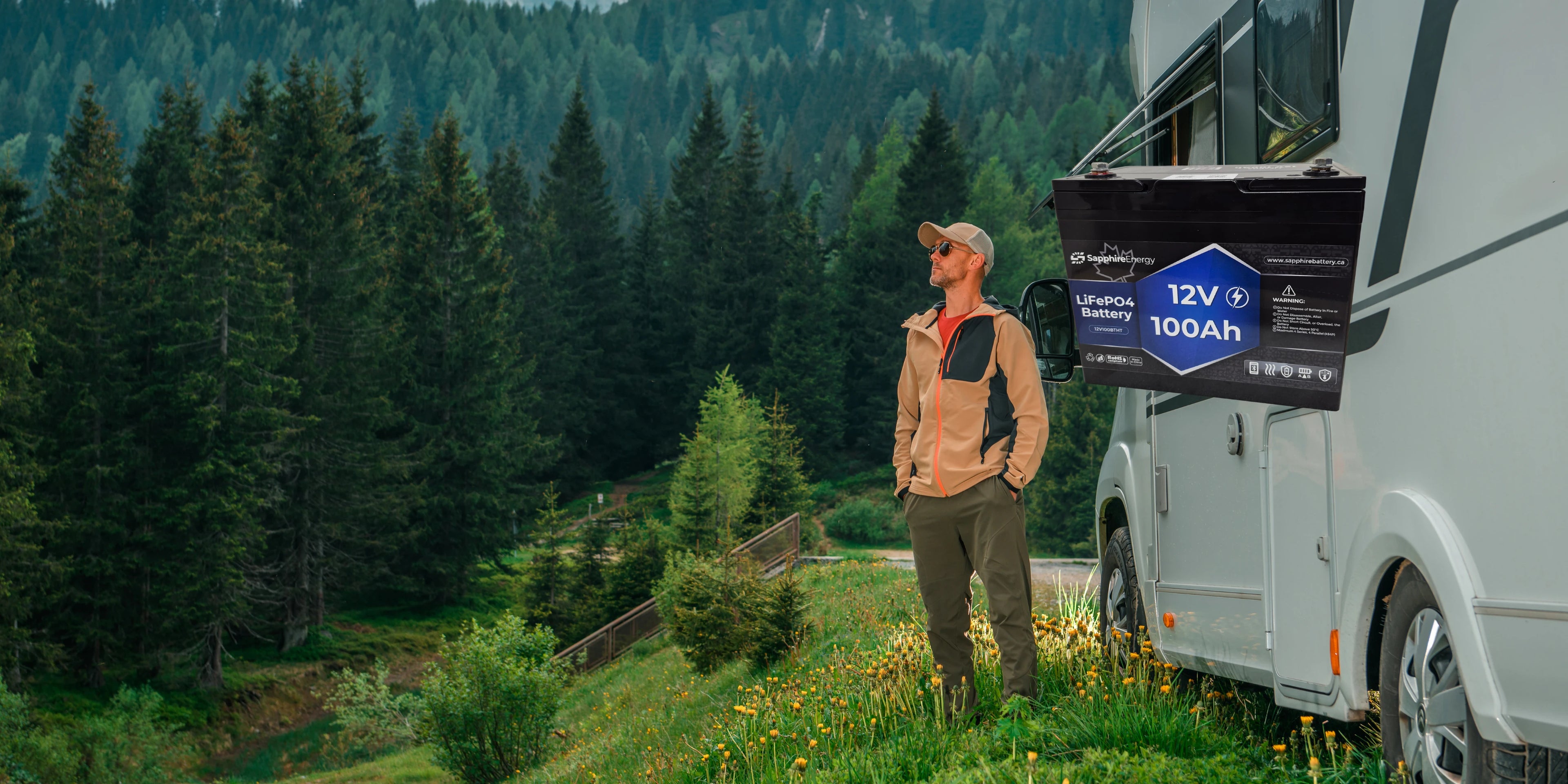 Man standing next to a camper van with a Sapphire Energy lithium battery pack labeled 12V 100Ah in a forest setting.